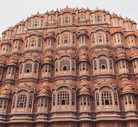 The Hawa Mahal in Jaipur uses Jharokhas - overhanging enclosed balconies that added architectural beauty and served a purpose. The palace was used by royal women to get a view of everyday life through the windows without being seen by the public. The honeycomb arrangement of balconies also allowed breeze to blow through the palace and kept it cool in the sweltering heat.